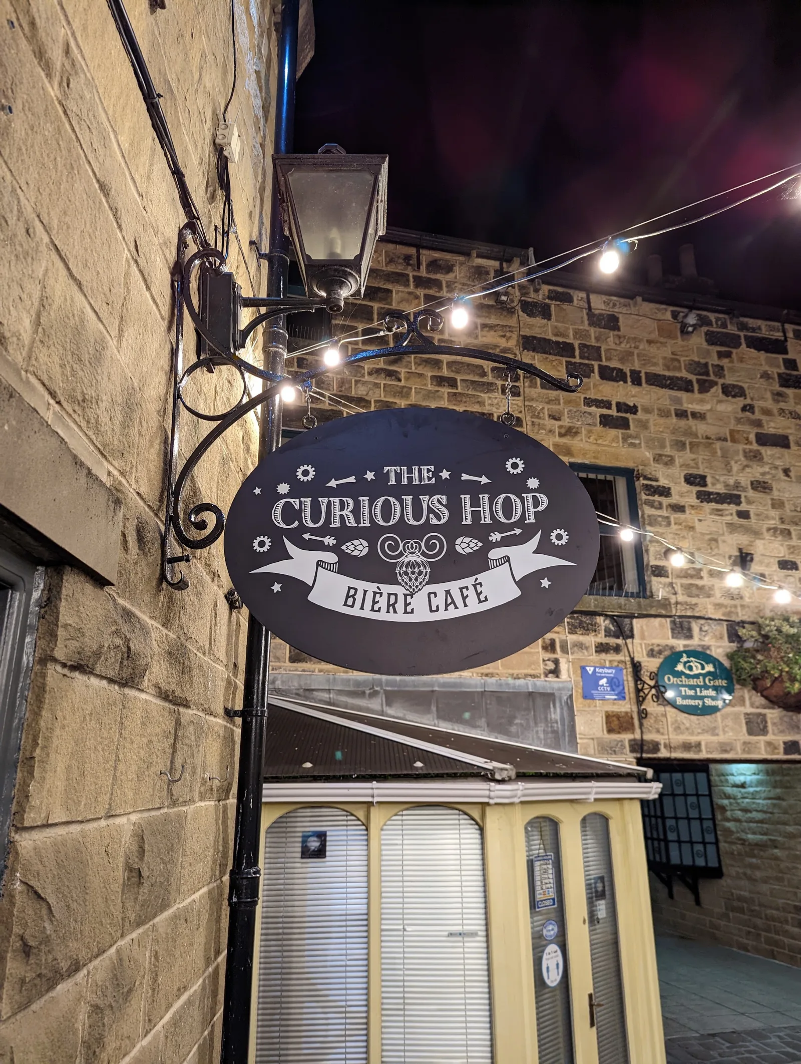 The ornate Curious Hop Bière Café hanging sign under the courtyard lights
